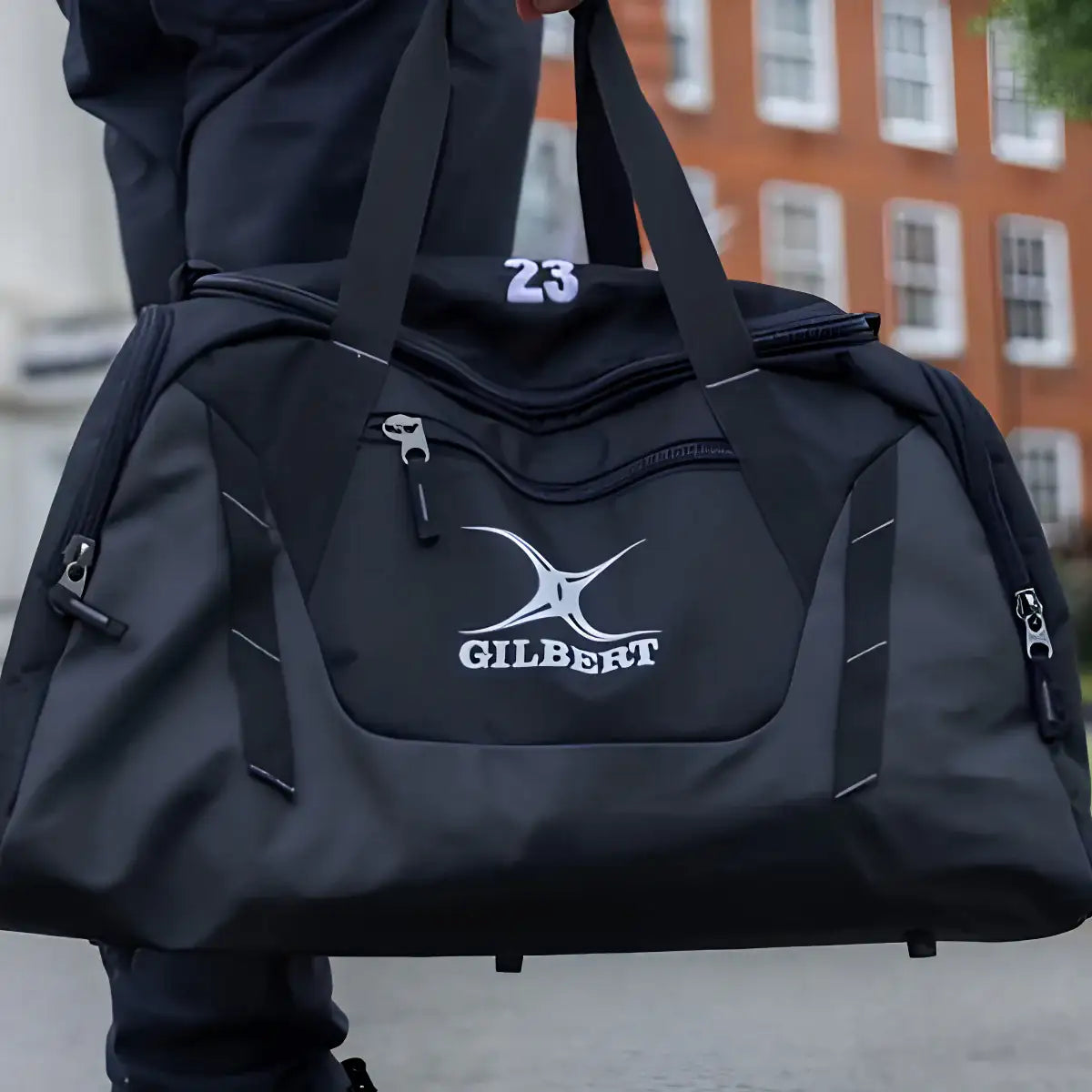 Black duffel bag with Gilbert logo held by a person outdoors.