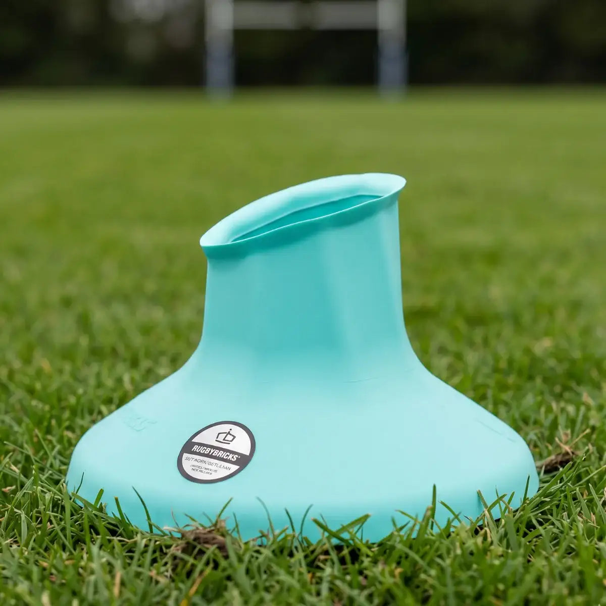 Turquoise RugbY brick Vortex kicking tee on grass with a brand logo
