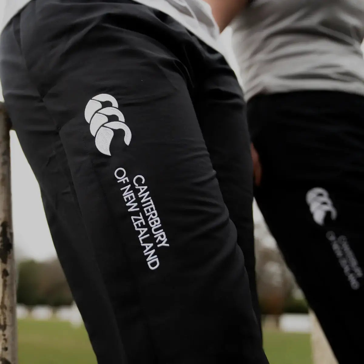 Black sports pants with Canterbury of New Zealand logo on a blurred outdoor background