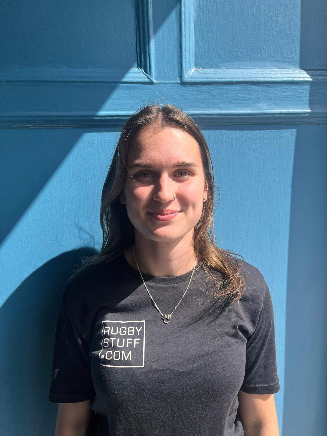 Rebecca Douglas wearing a black t-shirt with 'Rugby Stuff' logo against a blue wall